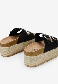 Sandales à plateforme noires avec deux brides ornées de boucles en argent. Texture naturelle semblable à de la corde sur la semelle, avec un coussin de pied en cuir tan.