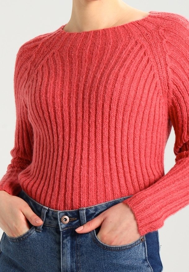 Pull en maille rouge côtelée avec un large col et des manches longues, présentant un tissu texturé et une coupe décontractée, assorti à un jean en denim bleu.