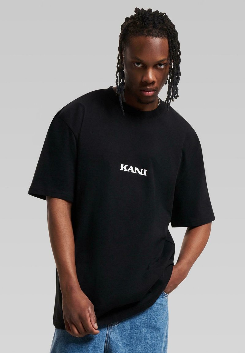 Black oversized t-shirt with short sleeves, featuring white "KANI" text on the front. The fabric appears smooth and casual in style.