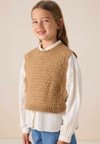 Gilet en tricot marron avec des bords festonnés porté sur une chemise blanche à manches longues. Le gilet présente un motif texturé et un détail de ourlet côtelé.
