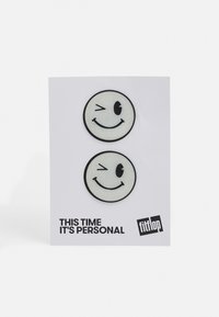 Dois patches de rostos sorridentes com contornos pretos em um cartão branco. Um pisca o olho; ambos têm uma textura brilhante. O texto diz "DESSA VEZ É PESSOAL."