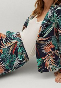 Marynarka i spodnie w kwiatowy wzór, z zielonymi i pomarańczowymi palmami na ciemnym tle. Materiał wydaje się gładki z detalami w postaci guzików.