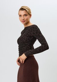 Schwarzes Langarmoberteil mit einem Leopardenmuster, das über gerüschte Details und eine enganliegende Silhouette verfügt, kombiniert mit einem braunen Rock.