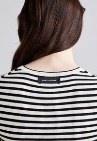 Fekete-fehér csíkos pulóver bordázott textúrával, kerek nyakkivágással és látható Marc Jacobs címkével a hátsó részén.