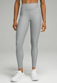 Legginsy sportowe o wysokim stanie, dopasowane, w jasnoszarym kolorze z teksturowanymi liniami. W połączeniu z białymi butami sportowymi, prezentującymi elegancki design.