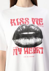 T-shirt bianco in cotone con una grande grafica di labbra nere, con testo rosso che recita "BACIAMI DOLCEMENTE" e "NON SPEZZARE IL MIO CUORE" sotto.