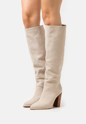 Knöchelhoche, beige Wildlederstiefel mit spitz zulaufender Schuhspitze, lässigem Design und einem gestapelten Holzabsatz. Glatte Textur mit minimalen Akzenten.