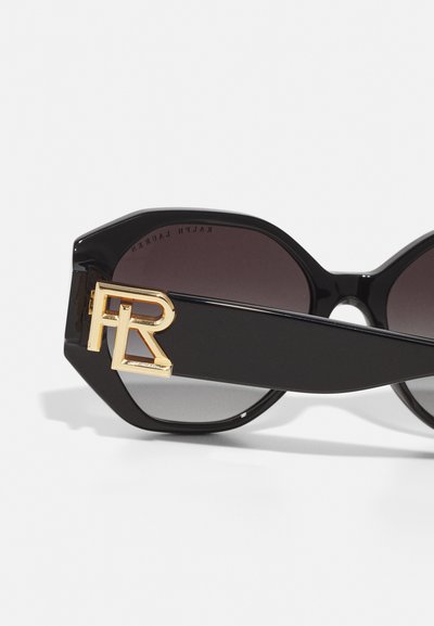 Black oversized sunglasses with tinted lenses, featuring a gold logo accent on the side. The frame has a geometric, angular design.