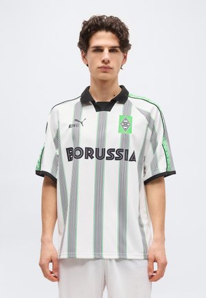 Jeune homme aux cheveux bouclés et foncés portant un maillot de football Borussia à rayures blanches et noires avec des détails verts et un col noir.
