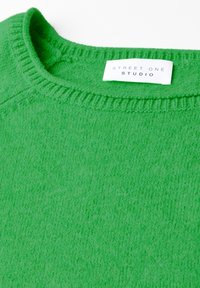 Grön stickad tröja med ribbad rundhals. Har en mjuk textur och en etikett som säger "STREET ONE STUDIO."