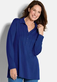 Blaues Langarm-Polohemd mit Knopfleiste, modischem Falten-Design und Kragen. Weicher Stoff mit lässiger Passform, kombiniert mit Jeans.