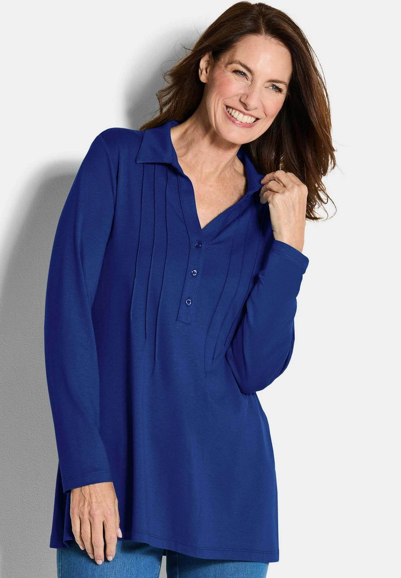 Blaues Langarm-Polohemd mit Knopfleiste, modischem Falten-Design und Kragen. Weicher Stoff mit lässiger Passform, kombiniert mit Jeans.