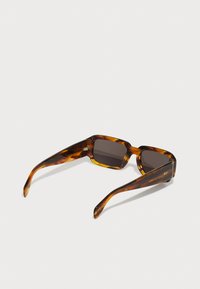 Gafas de sol de carey marrón con montura rectangular, lentes oscuros y brazos ligeramente curvados. Presentan un detalle grabado en la patilla.