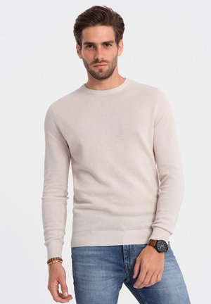 Lichtbeige gebreide trui met een ronde hals en lange mouwen. Heeft ribgebreide manchetten en een ribgebreide zoom. Gedragen met denim jeans en een horloge.