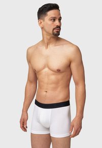 Hvite boxer-truser med en svart elastisk midje. Laget av glatt stoff med en tettsittende design og en kontrasterende merkevarelogo på midjen.