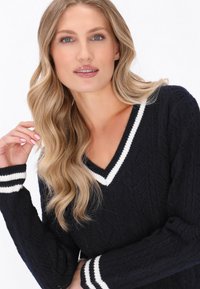 Marine gebreide trui met een V-hals, witte gestreepte ribbenaccenten op de halslijn en manchetten, en een gestructureerd patroon doorheen.