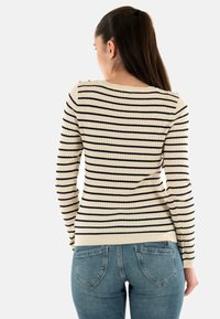 Maglione a maniche lunghe a coste color crema con righe blu navy, con dettagli sulle spalle. Abbinato a jeans azzurri, con un focus su trame e motivi.