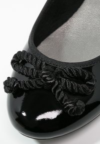 Ballerine en cuir verni noir avec un nœud en corde torsadée sur l'embout arrondi et un bord en tissu autour de l'ouverture.