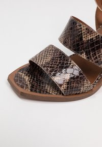 Öppen tå sandaler med ett ormprint i brunt och svart, med tre breda remmar och en brun gummisula.