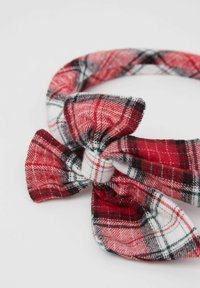 Červená a bílá kostkovaná látková čelenka s mašlí, s jemnou texturou a černými akcenty v designu. Kulatý tvar.