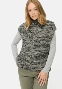 Gilet en tricot en fils gris et noir marbrés, avec un col montant et des manches courtes, superposé sur un haut gris à manches longues.