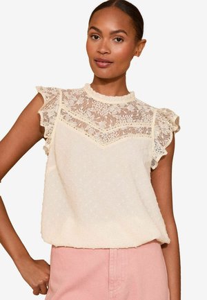 Blusa color crema con dettagli in pizzo, maniche a volant e texture a pois. Presenta un collo alto e una vestibilità morbida.