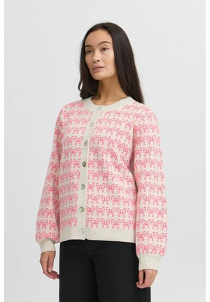 Cardigan rose clair avec un motif de nœuds répétitif, des poignets côtelés, un col rond et une fermeture à boutons à l'avant avec de gros boutons.