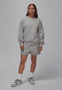 Grå bomullssweatshirt med rund hals og Jordan-logo, sammen med matchende grå shorts. Hvite sportssokker og grå joggesko fullfører antrekket.
