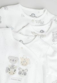 Biele detské body so zvieracími motívmi, z jemného bavlneného materiálu, so zapínaním na patentky a výšivkou zvieracích tvárí na jednom kuse. Viditeľné sú vzory s bodkami.