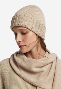 Beżowa dzianinowa czapka z prążkowanym wzorem i subtelnymi cekinowymi akcentami, zestawiona z miękkim beżowym szalikiem, prezentująca gładką teksturę i ciepło.