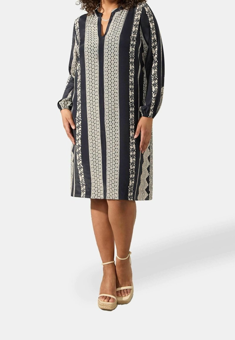 Tummansininen mekko, jossa on kukkakuvioita ja raidallista kuosia, kolmivartiset hihat ja lovikaulus. Yhdistetty beigeihin platform-sandaaleihin.