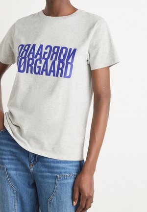 Personne portant un t-shirt gris clair avec un texte miroir bleu audacieux "NORGAARD ORGAARD" associé à un jean bleu en denim.