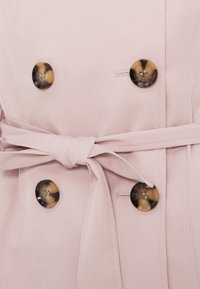 Ροζ παλτό τρεντσκότ με μεγάλα, στρογγυλά κουμπιά σε σχέδιο χελώνας και ζωνάκι από το ίδιο ύφασμα. Με λεία υφή και κομψό, προσαρμοσμένο σετ.