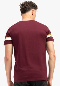 Tamsiai raudona medvilninė marškinėliai, su trumpomis rankovėmis ir baltomis bei geltonomis juostomis ant pečių, bei apvalia iškirpte.