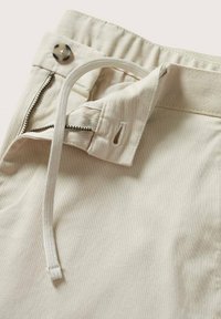 Pantalon beige avec braguette zippée et ceinture à cordon, doté d'un bouton décoratif et d'une texture de tissu lisse.
