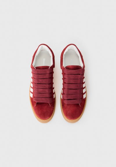 Red suede sneakers with prominent lacing, white stripes on the sides, and a gum sole. Features a cushioned interior for comfort.