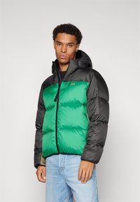 Chaqueta acolchada con un cuerpo verde brillante y mangas negras, que cuenta con capucha, cremallera frontal y un pequeño logo en el pecho.