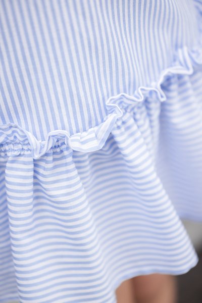 Υφασμα με μπλε και λευκές ρίγες και βολάν στο τελείωμα. Η υφή είναι λεία, με οριζόντιες ρίγες και ρυτιδώσεις στη μέση.