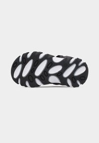 Μαύρη και λευκή σόλα από καουτσούκ ενός αθλητικού σανδαλιού, με την κάτω πλευρά να κοιτάζει προς τα πάνω, που δείχνει υφή με οβάλ σχέδιο πέλματος σε απλό φόντο.