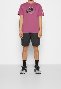 Burgundy Nike t-shirt med logga, grå shorts, svarta Nike-strumpor och flerfärgade sneakers. Enkelt design, avslappnad passform, bomullsmaterial.