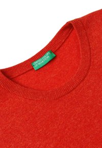 Czerwona dzianinowa sweter z prążkowanym okrągłym dekoltem i zieloną metką United Colors of Benetton wszytą w kołnierz.