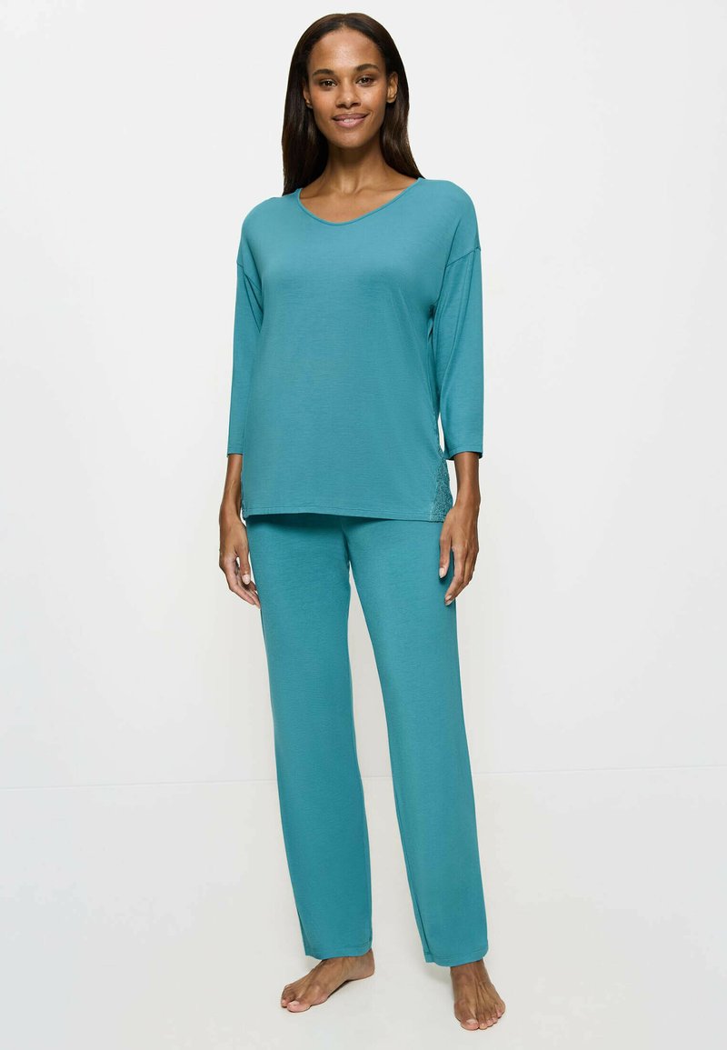 Completo loungewear color teal caratterizzato da un collo a V, maniche a tre quarti e pantaloni larghi con una texture liscia e una silhouette rilassata.