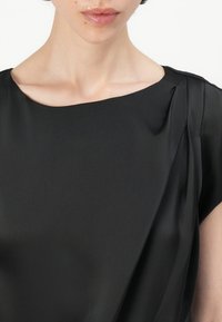 Blusa negra de satén con escote redondo, textura drapeada, mangas cortas y un detalle de plisado sutil en un hombro.