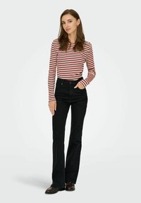 Zwarte flare jeans met een hoge taille, gecombineerd met een rood-wit gestreepte lange mouwen top. Model staat met een hand in de zak.