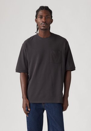Dunkelgraues T-Shirt mit kurzen Ärmeln und rundem Ausschnitt sowie einer Brusttasche auf der linken Seite; glatte Baumwolltextur; lockere Passform, kombiniert mit blauen Jeans.