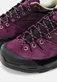 Fialové semišové turistické topánky s čiernymi textilnými doplnkami a textúrovanými gumovými podrážkami. Majú zosilnené očka na šnúrky a kontrastné detaily šnúrok.
