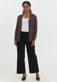 Cardigan en tricot bourgogne sur une chemise blanche, associé à un pantalon large noir et des chaussures à talons noires, présentant une coupe décontractée et un design à l'avant ouvert.