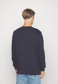 Sudadera azul marino de manga larga, con cuello redondo y puños de canalé. La tela parece suave con una textura lisa.