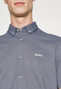 Koszula na guziki w ciemnoniebieskim kolorze z teksturowanym wzorem. Posiada zaostrzony kołnierzyk oraz srebrne logo "BOSS" na piersi.