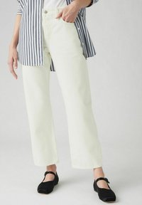 Lichtgele wide-leg jeans met een hoge taille, zijzakken en een klassieke knoopsluiting, gecombineerd met zwarte schoenen en een gestreept shirt.